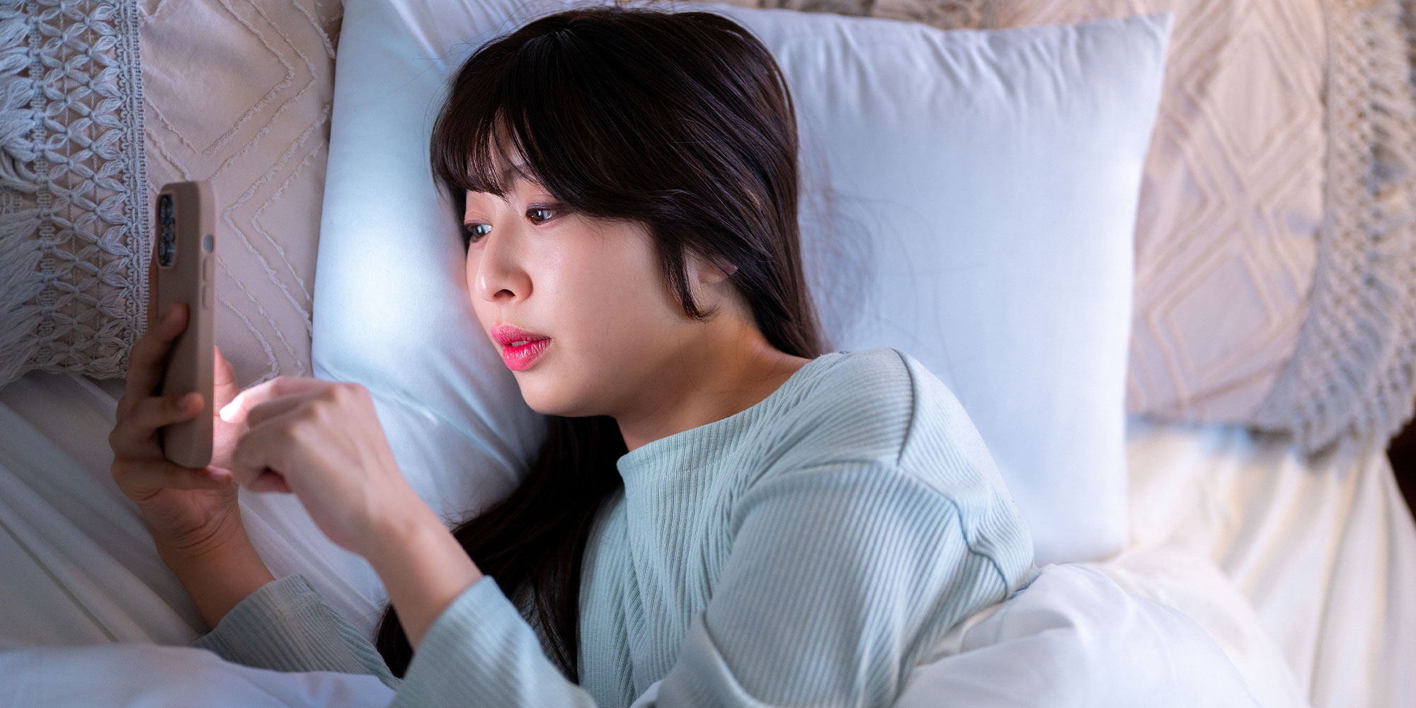 寝床でスマートフォンを使う女性