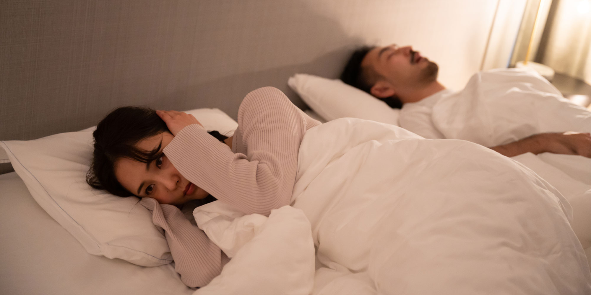 いびきをかいて眠る男性とうるさくて眠れない女性