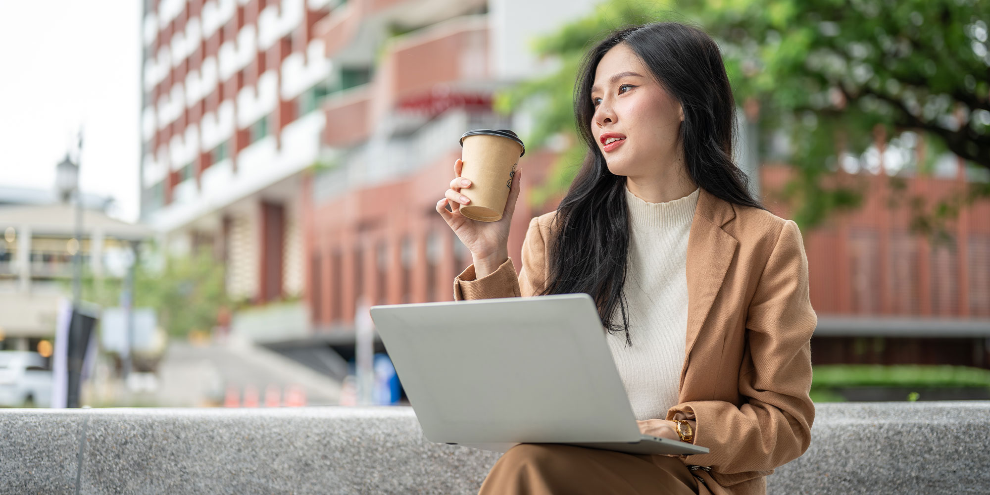 コーヒーとパソコンを持って公園に居る女性